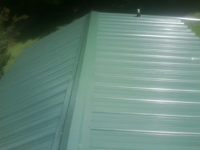 New green metal panels meeting at the ridge of a roof — Flat Roof Repair work by our crew in Fletcher
