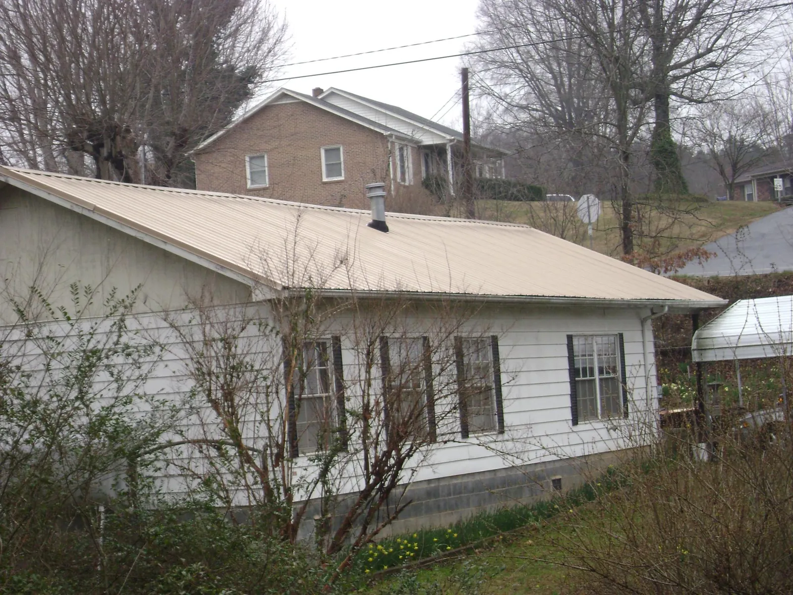 Tan metal roof on a white sided house set into a hillside — Commercial Roofing by Roofing Brothers in Fletcher